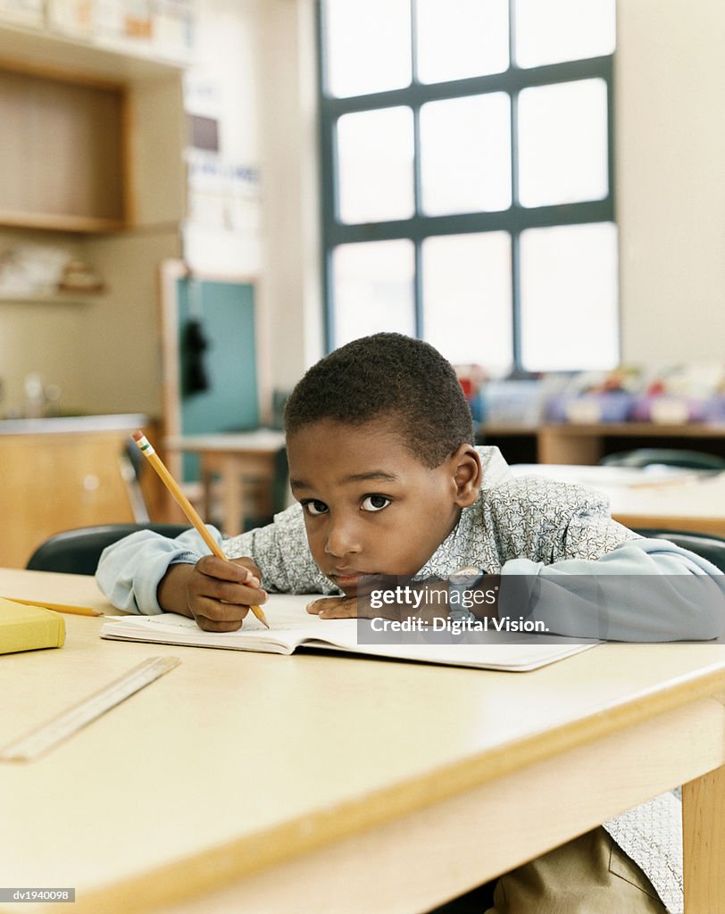 Bored Looking Schoolboy Sitting at a Table and Resting His Head on a Exercise Book