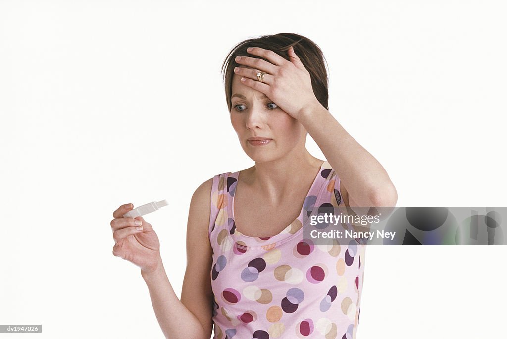 Young Woman Looks at a Pregnancy Test, Her Hand on Her Head in Panic