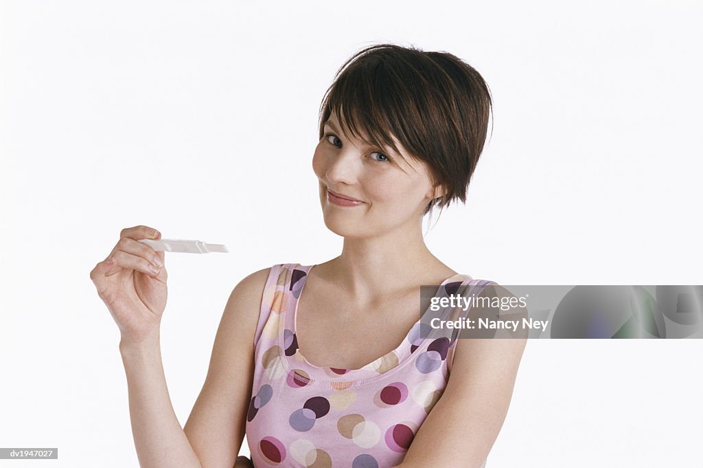 Studio Shot of a Young Woman Holding a Pregnancy Test and Smiling