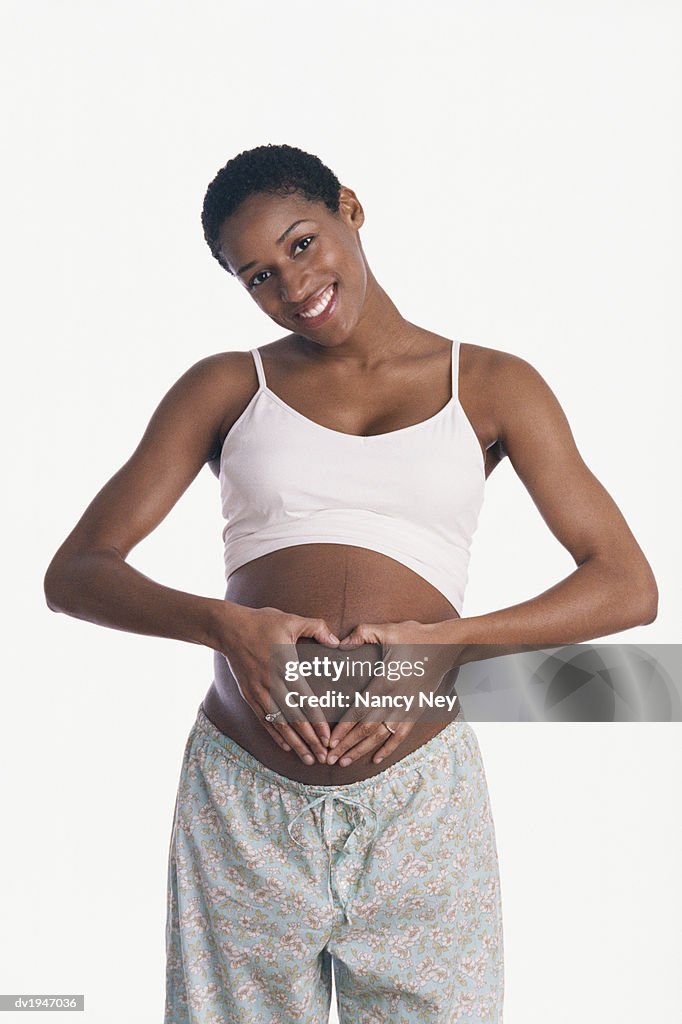 Studio Portrait of a Pregnant Woman Making a Heart Shape With Her Hands on Her Stomach