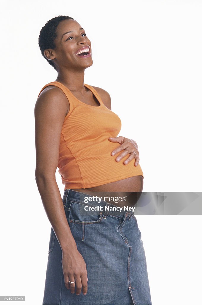 Studio Shot of a Pregnant Woman in a Vest and Denim Skirt, Laughing