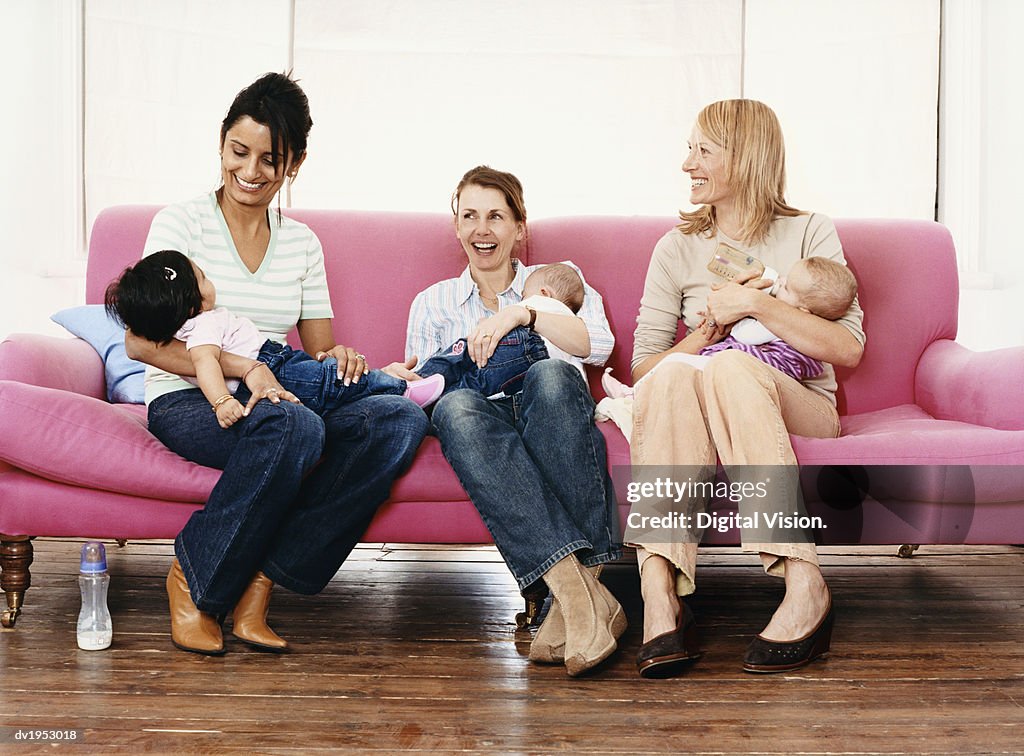 Young Mothers with Their Babies on a Pink Sofa
