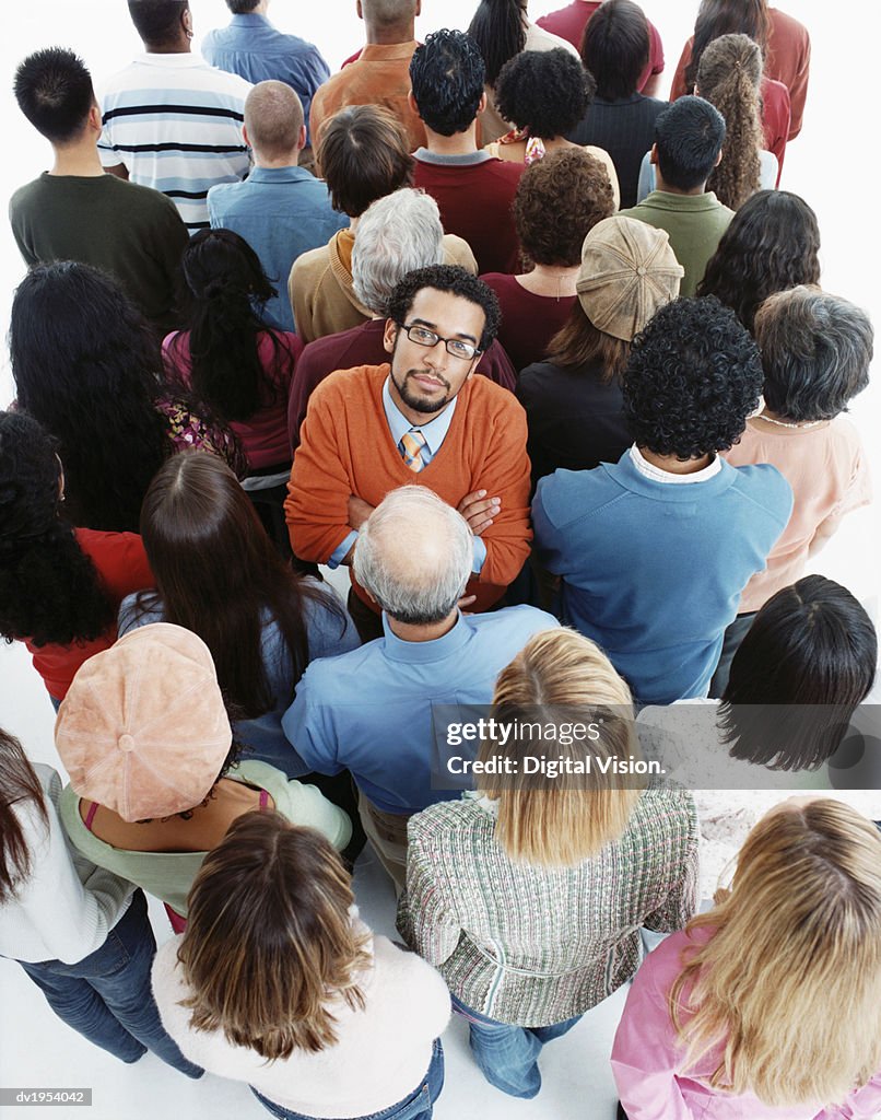 Elevated Studio Shot of a Well Dressed Man Standing in a Crowd of People With Their Backs Turned, Looking at the Camera