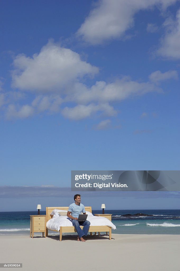 Man Sits on a Bed at the Edge of the Sea Using a Laptop