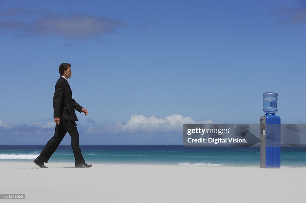 Businessman Walking Towards a Water Cooler on a Beach