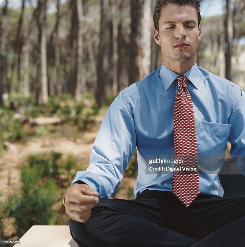 Well-Dressed Businessman Sits in a Forest, Meditating in the Lotus Position