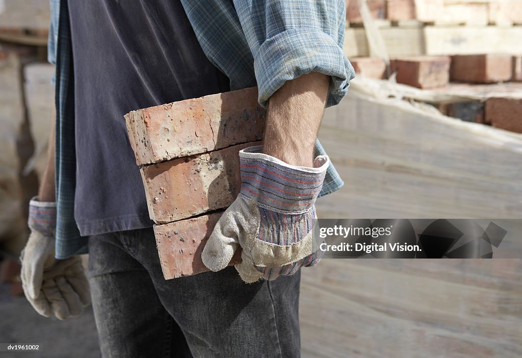 Mid Section of a Bricklayer Carrying Three Bricks With Protective Gloves
