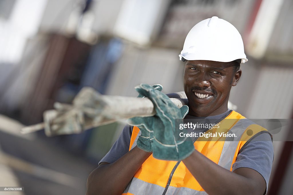 Portrait of a Builder Wearing a Hard Hat Carrying Scaffolding Poles Over His Shoulder