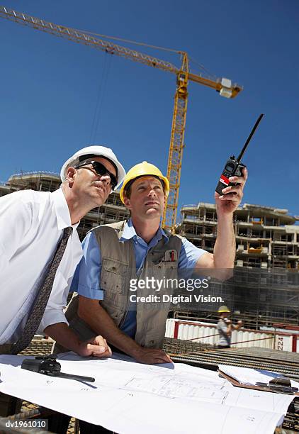 well dressed man wearing sunglasses standing side by side with a building site foreman, who is pointing with a walkie talkie - foreman stock pictures, royalty-free photos & images