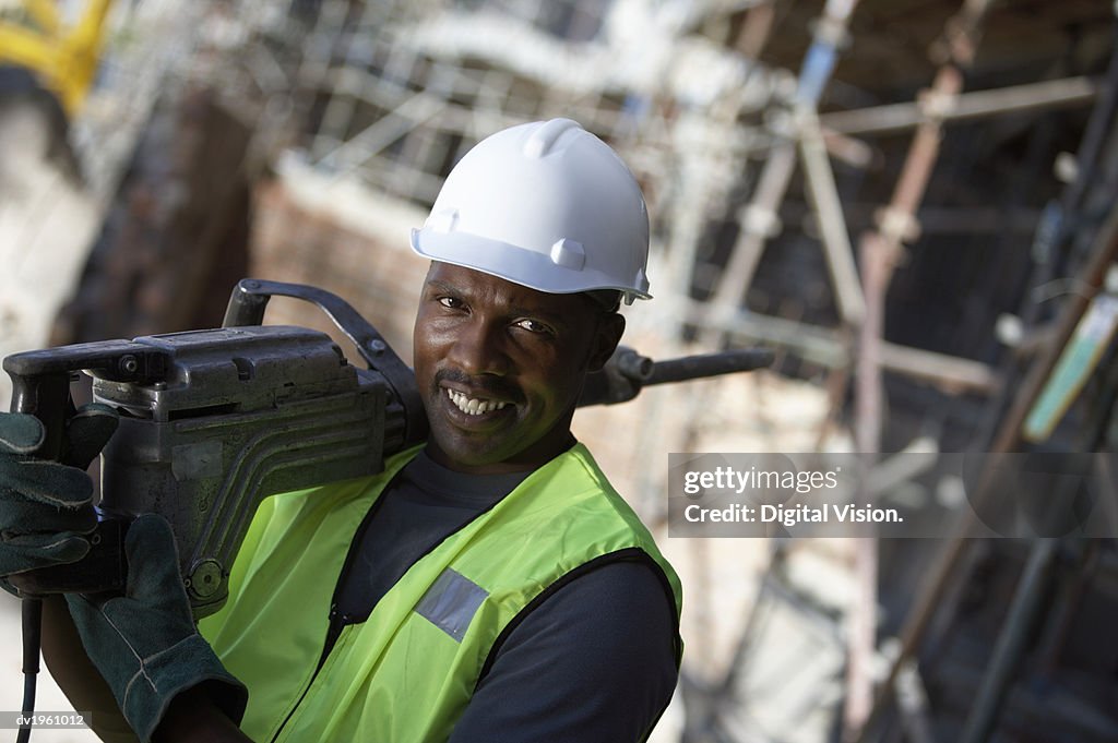 Portrait of a Male Builder in a Hard Hat, Carrying a Drill on His Shoulder