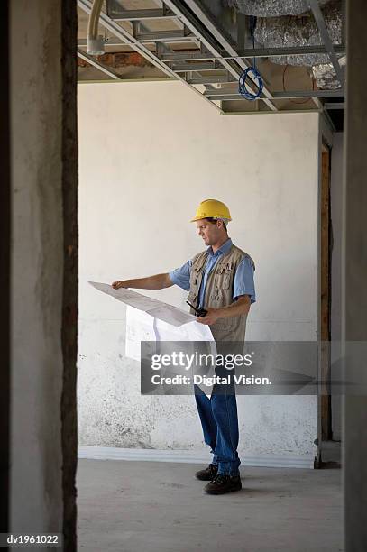 foreman stands in a building site examining a blueprint - foreman stock pictures, royalty-free photos & images