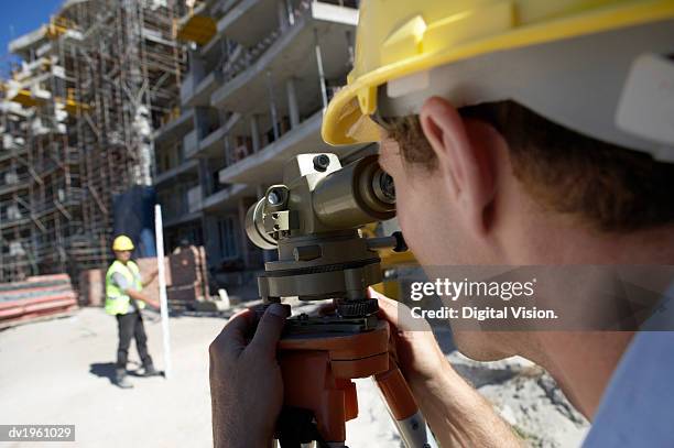 surveyor looking through a theodolite, on a building site - geodesy stock pictures, royalty-free photos & images