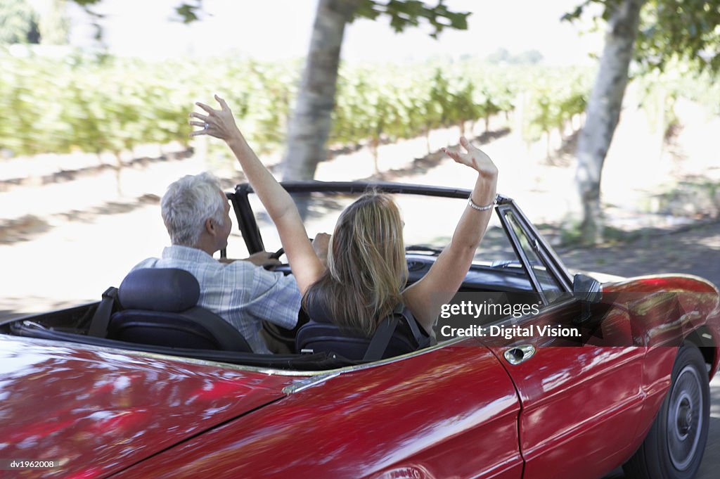 Rear View of a Couple in a Red Convertible, the Woman With Her Arms in the Air