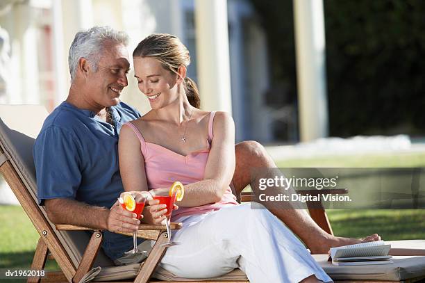 affectionate couple sit on a sun lounger holding cocktail glasses - age contrast stock pictures, royalty-free photos & images