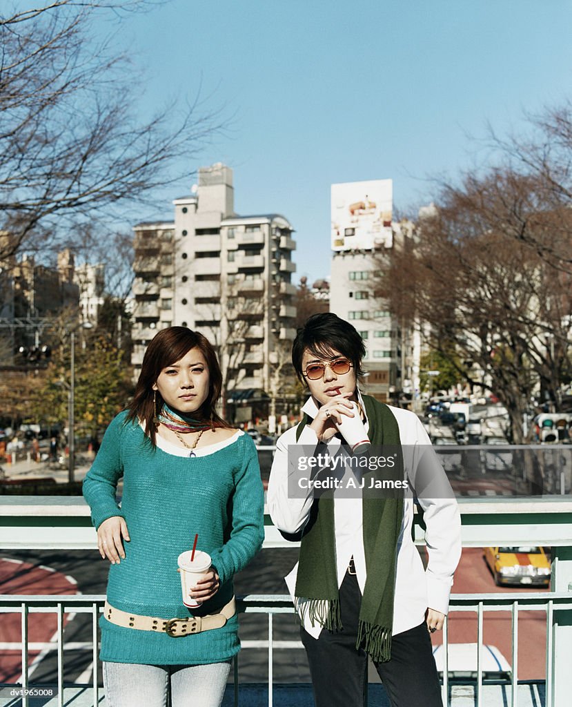 Couple Leaning Against a Railing Drinking From Disposable Cups