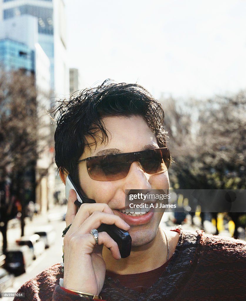 Young Man Outdoors in the City Using a Mobile Phone Wearing Sunglasses