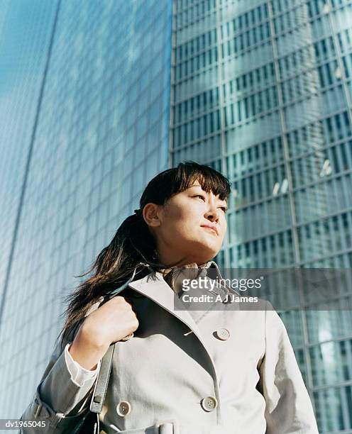 low angle shot of a young woman wearing a mackintosh with an office block in the background - j mac stock pictures, royalty-free photos & images