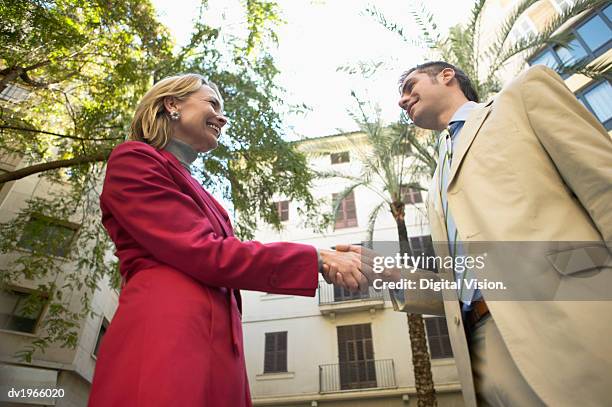 businesswoman and businessman stand outdoors, shaking hands - low angle view of two businessmen standing face to face outdoors stock pictures, royalty-free photos & images