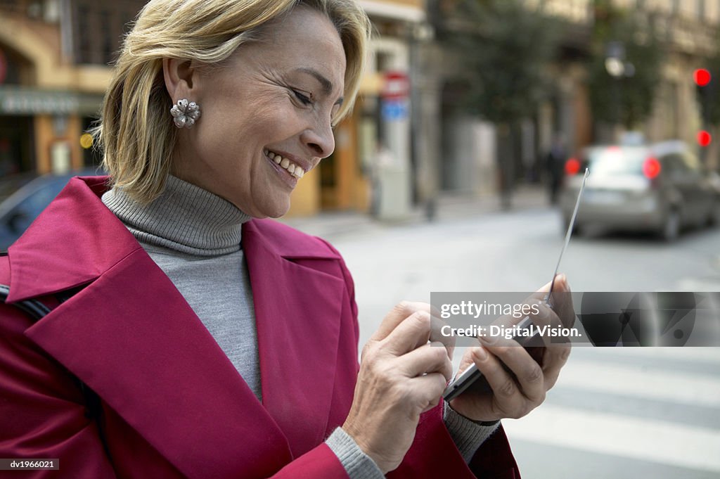 Woman Standing Outdoors Using a Mobile Phone and a Stylus