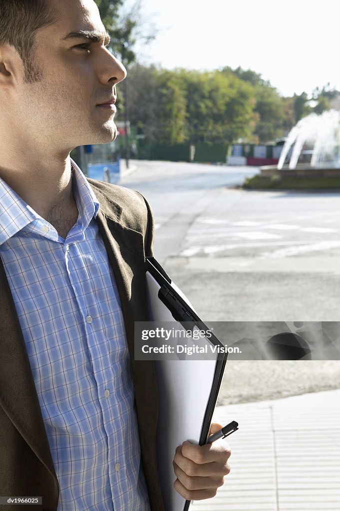 Smartly Dressed Man Holding a Clipboard, Standing in an Urban Setting