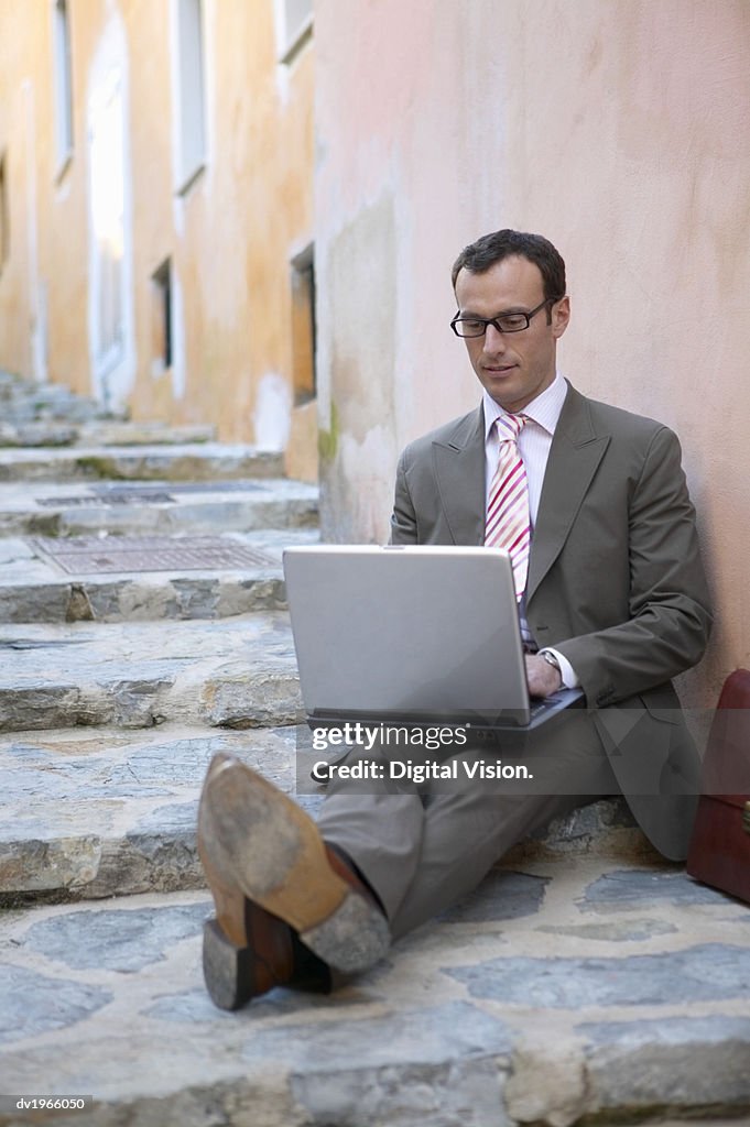 Businessman Using a Laptop Sitting on Steps on the Pavement