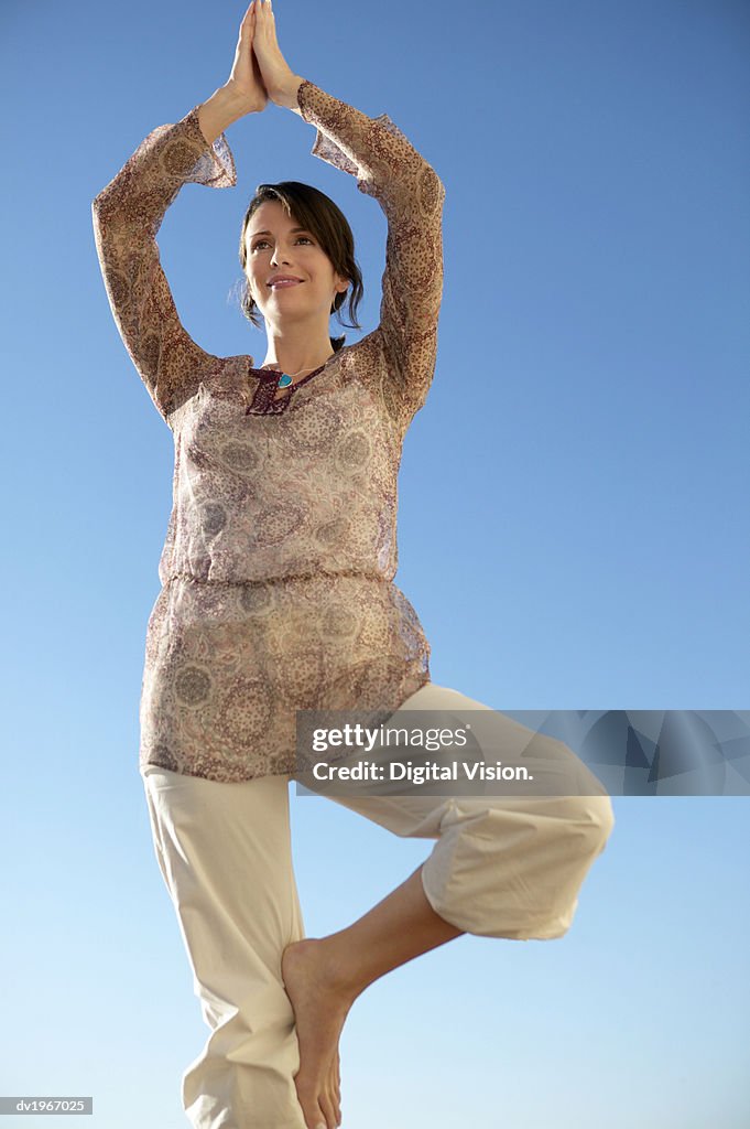 Woman Stands Outdoors in a Yoga Position, On One Leg With Her Arms Above Her Head