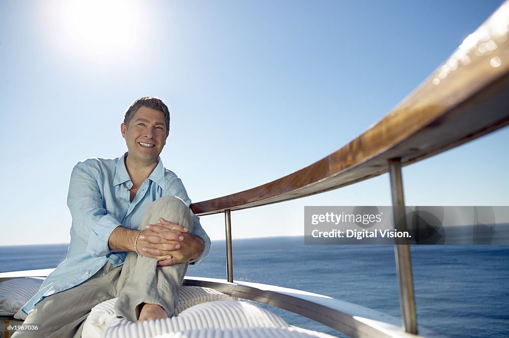 Smiling Man in Casual Summer Clothing Sits on a Sunlit Balcony by the Sea