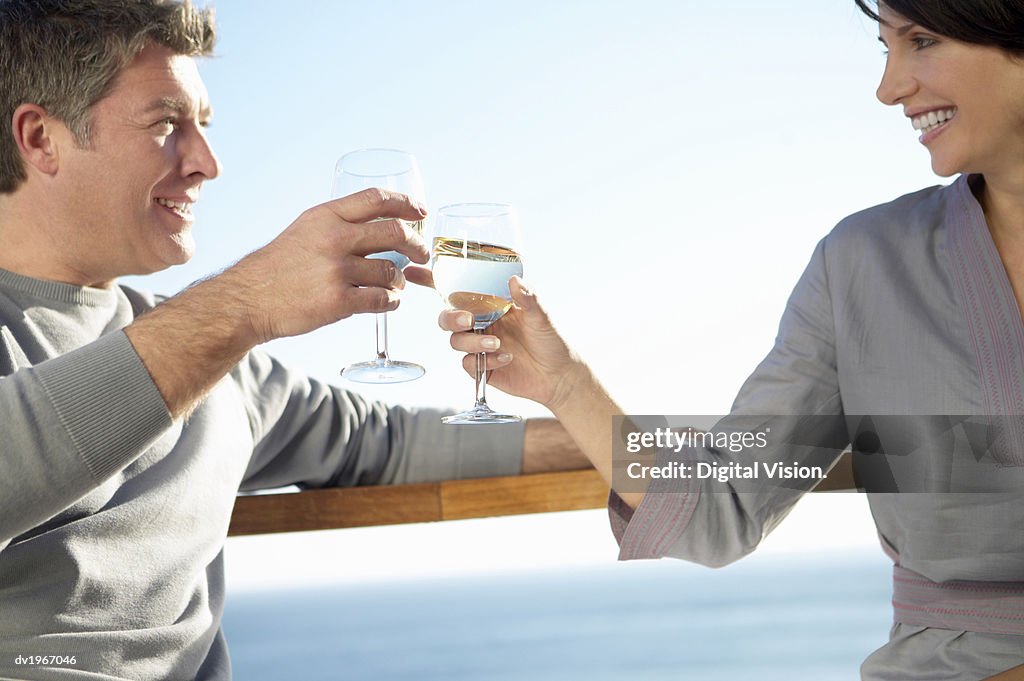 Couple Stand on a Balcony Making a Toast With Glasses of White Wine