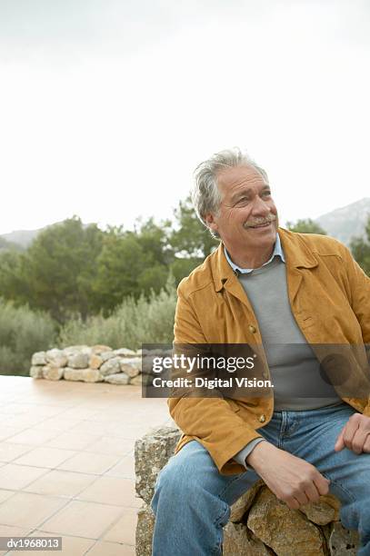 senior man sitting on a stone wall on a terrace - suede jacket stock pictures, royalty-free photos & images