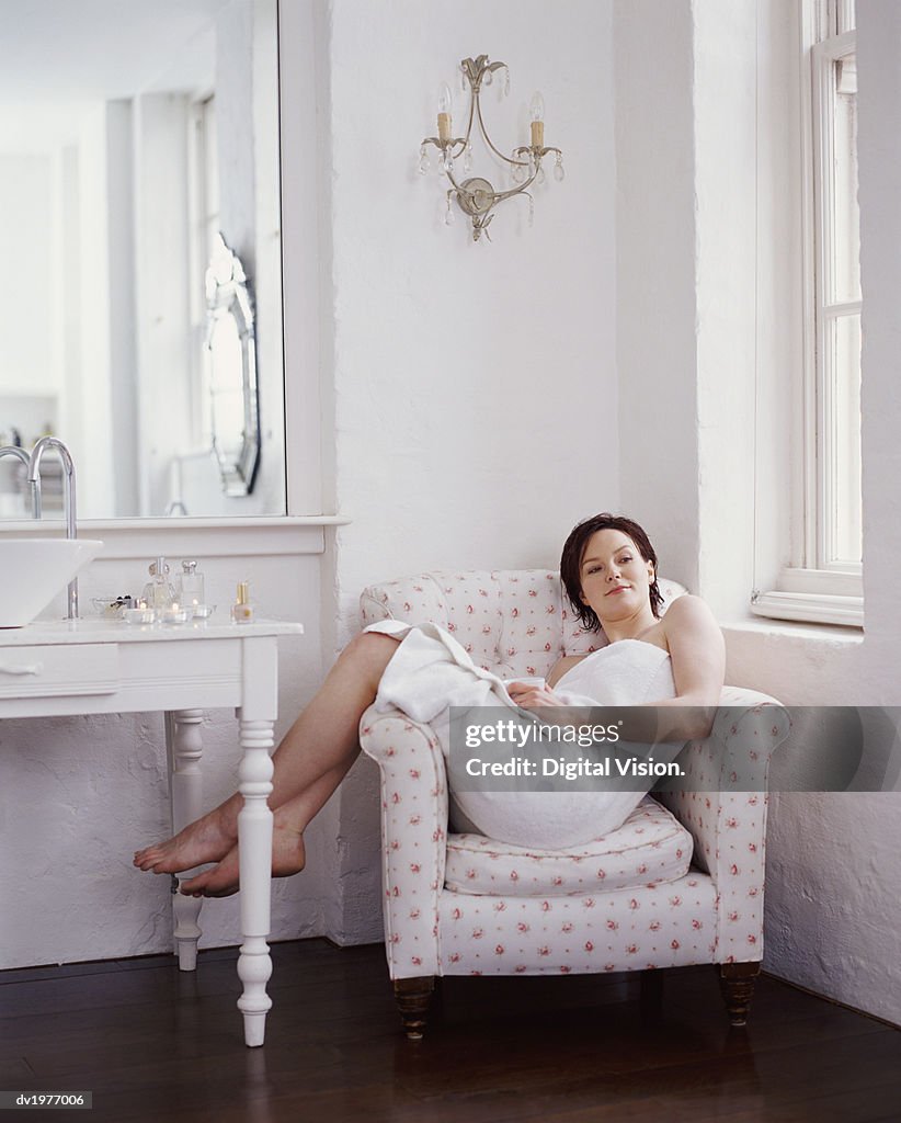 Young Woman Wrapped in a Towel Sitting in an Arm Chair in a Bathroom