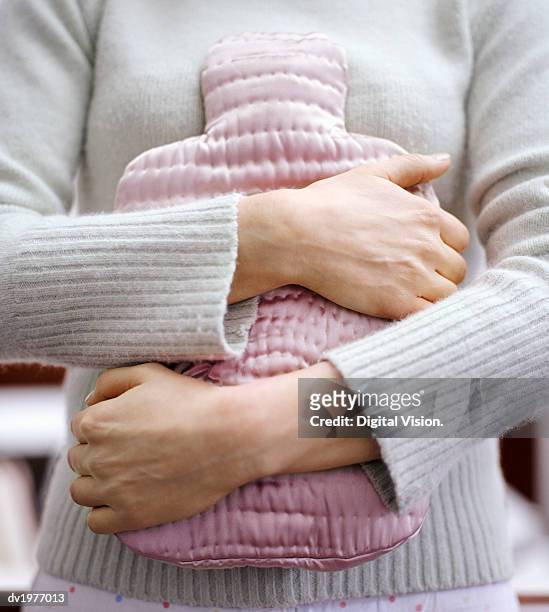 mid section shot of a woman holding a pink water bottle against her stomach - hot water bottle stock pictures, royalty-free photos & images