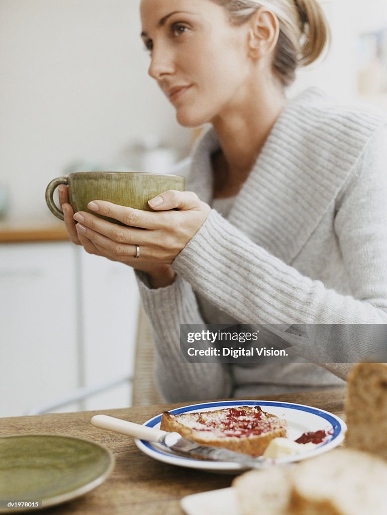 Woman Sits at a Table Holding a Cup, Plate With Toast on Table