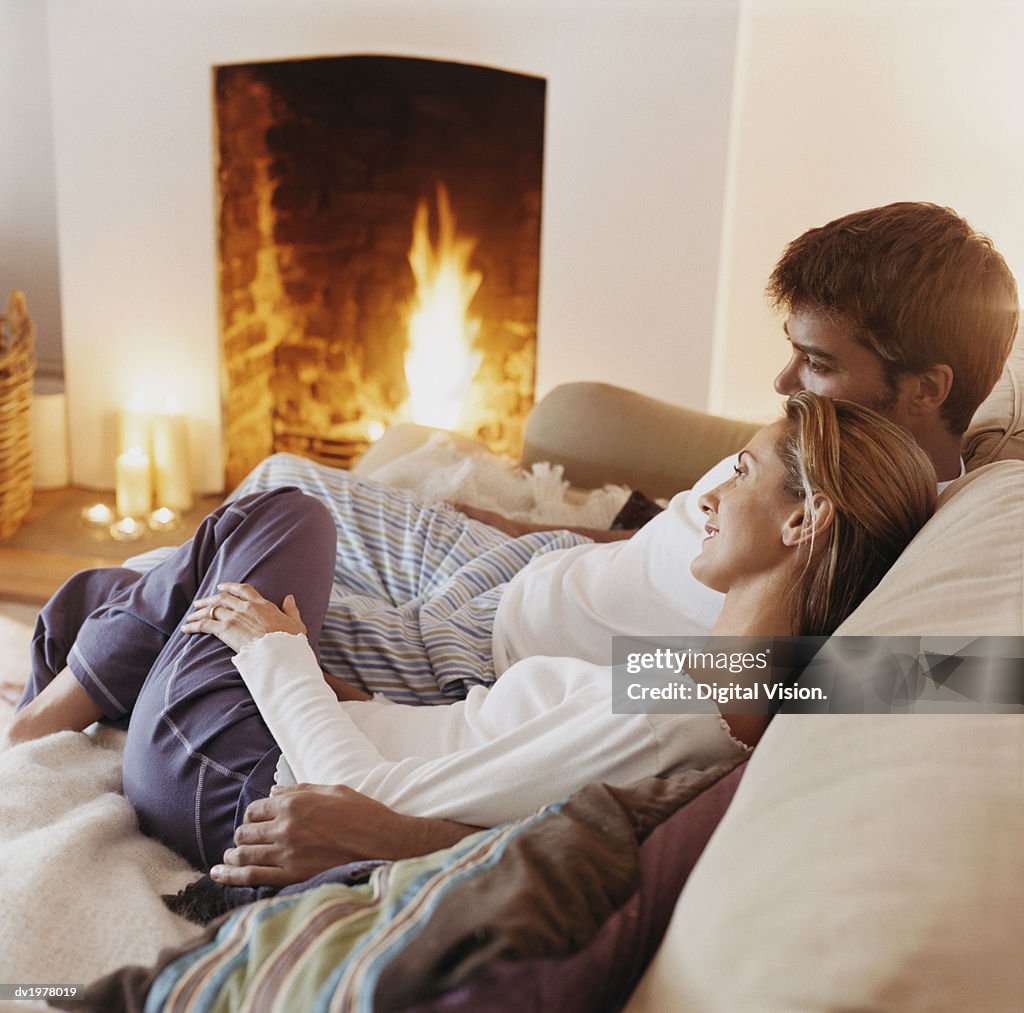 Couple Sitting Close to Each Other on a Sofa by a Fireplace