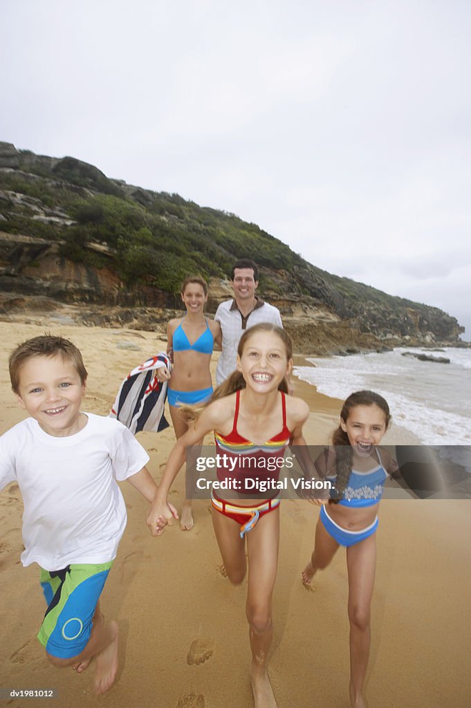 Young Girls and a Boy Run Along the Beach in Front of Their Parents