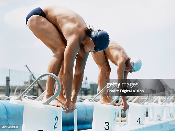 two men standing side by side on starting blocks at a swimming pool - swimming starting block stock pictures, royalty-free photos & images