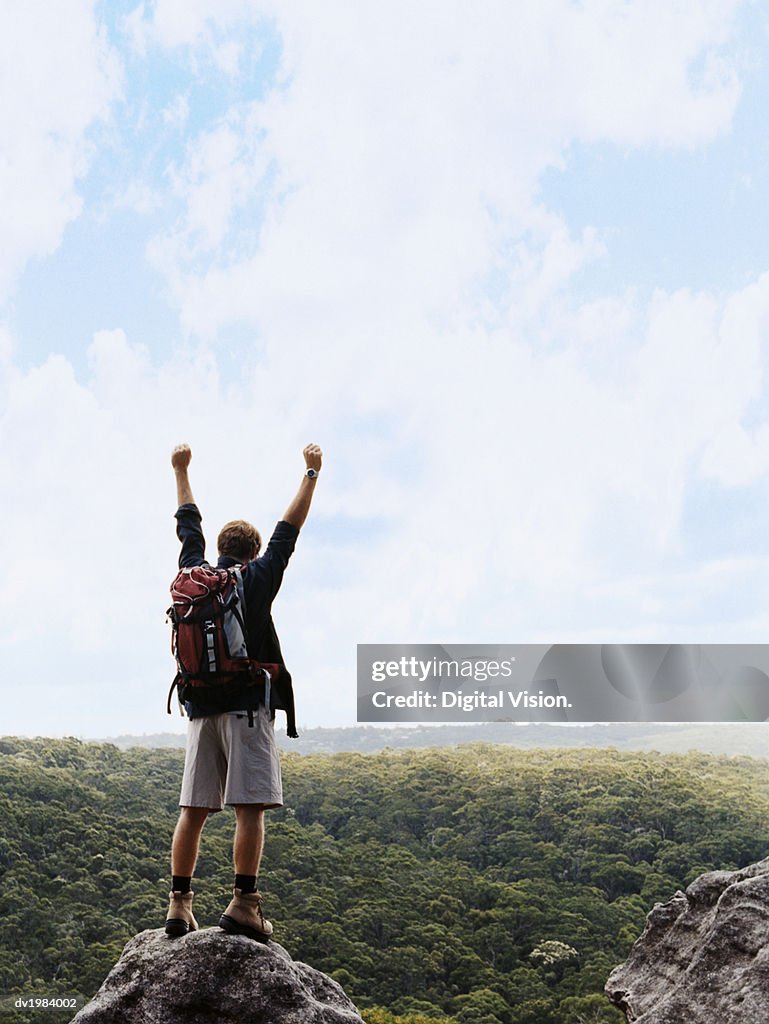 One Man Standing on Top of a Rock With his Arms Up