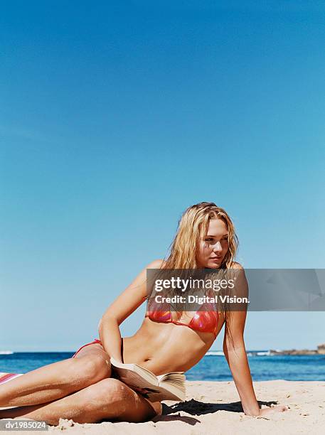 young woman sitting on a beach and holding a book - acostado de lado fotografías e imágenes de stock