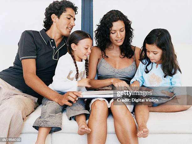family sitting together on a sofa and looking at a photo album - digital twin bildbanksfoton och bilder
