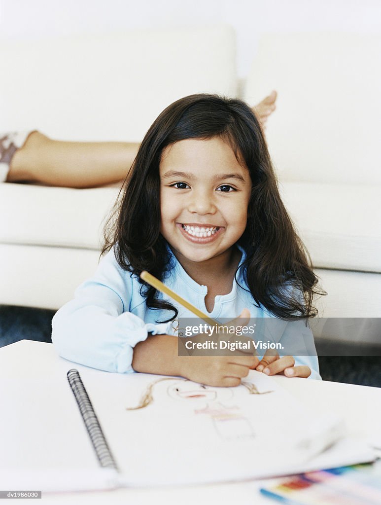 Portrait of a Smiling, Young Girl With a Drawing Book at a Table