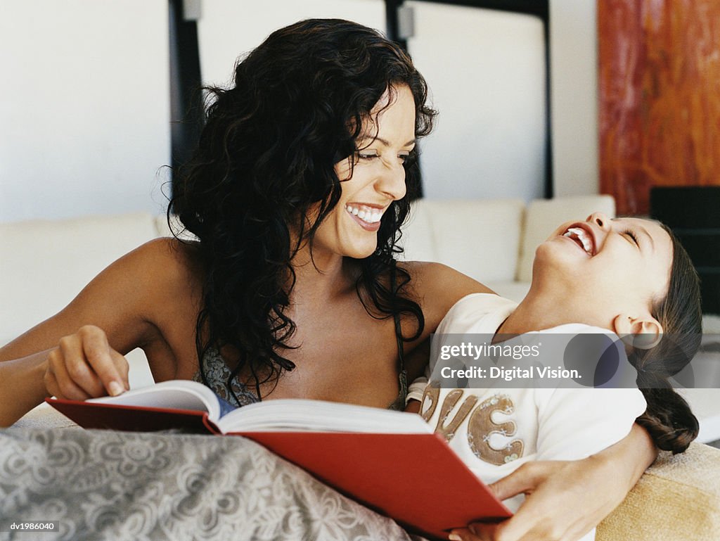 Young Girl Laughing as Her Mother Reads a Book to Her