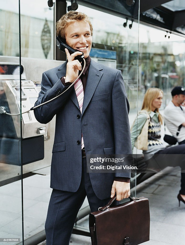 Businessman Stands by a Bus Stop Talking on a Payphone