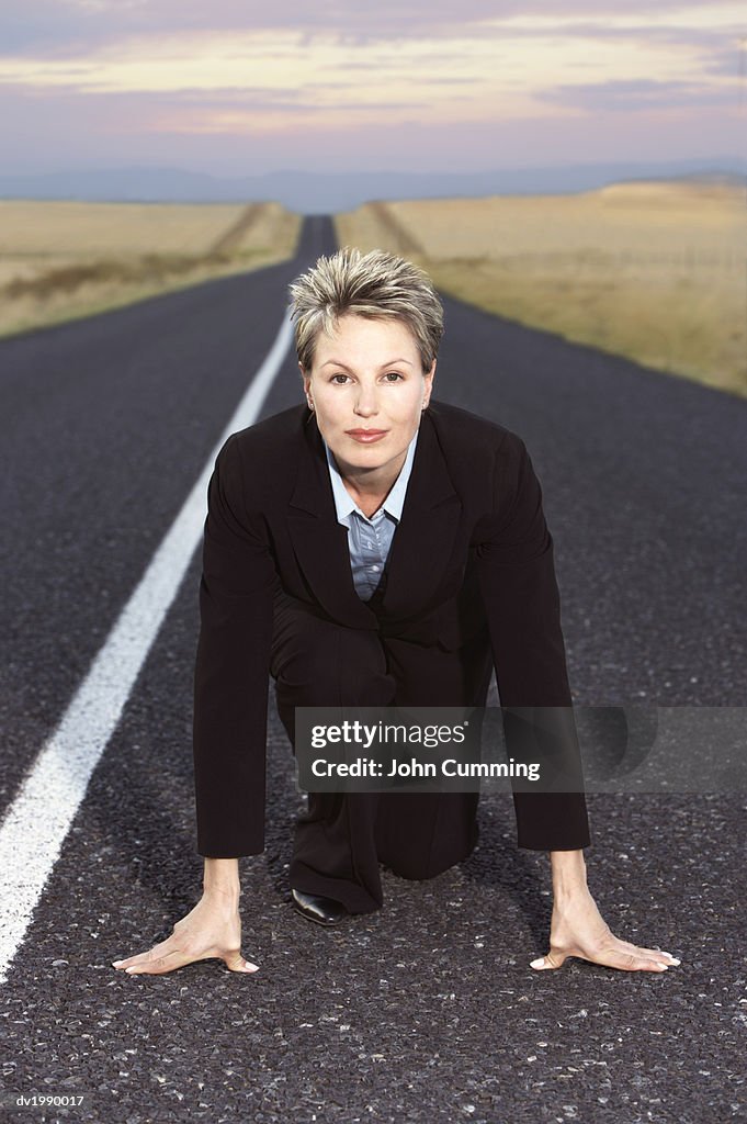 Businesswoman Kneeling on a Remote Road in Preparation for a Race