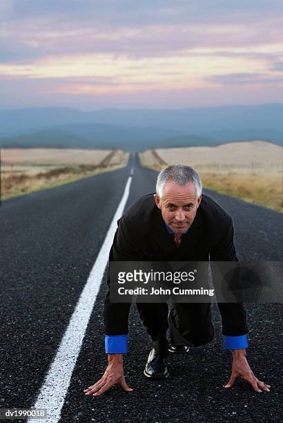 businessman kneeling on a remote road in preparation for a race - crossing the road stock pictures, royalty-free photos & images