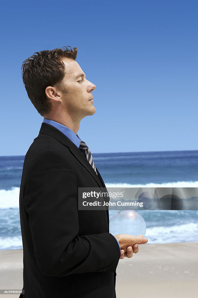 Businessman Standing on a Beach and Holding a Sphere in His Cupped Hands