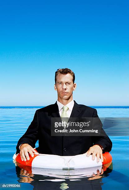 businessman floating in the sea with a rubber ring - rubber ring stock-fotos und bilder
