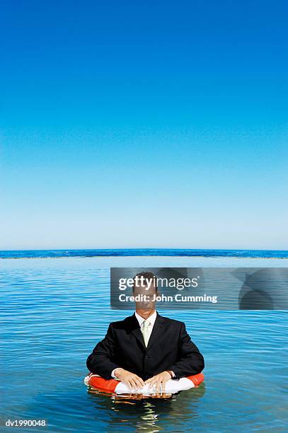 businessman wearing a full suit and floating in the sea with a rubber ring - rubber ring stock-fotos und bilder