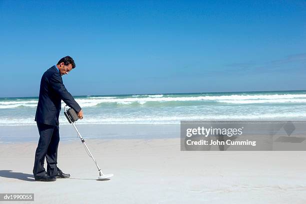 businessman using a metal detector on a beach - needle in a haystack 英語の慣用句 ストックフォトと画像