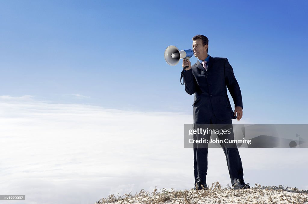 Businessman Standing on a Sand Dune and Shouting Into a Megaphone