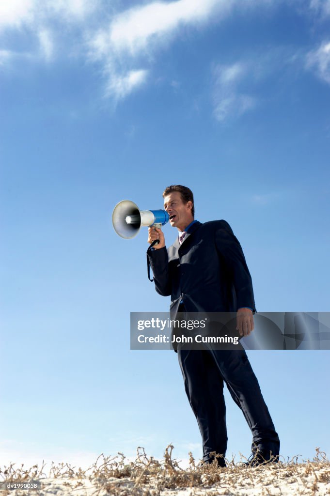 Businessman Standing on a Sand Dune and Shouting Into a Megaphone