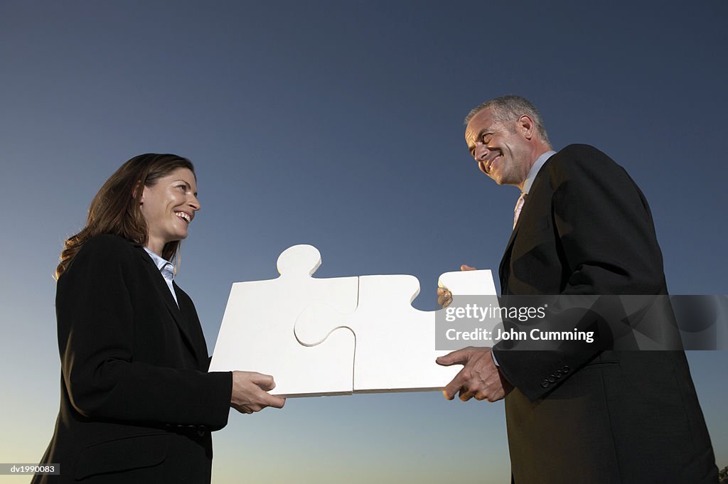 Businessman and Businesswoman Connect Two Large Jigsaw Pieces